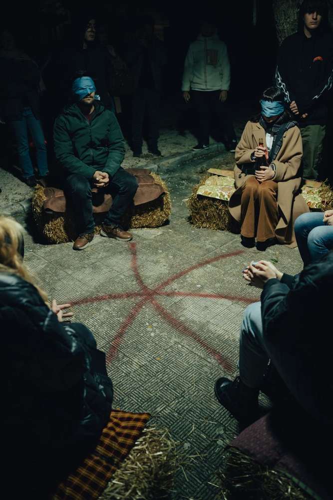 A red sign sprayed on the ground, the blindfolded audience seated around it A red sign sprayed on the ground, the blindfolded audience seated around it