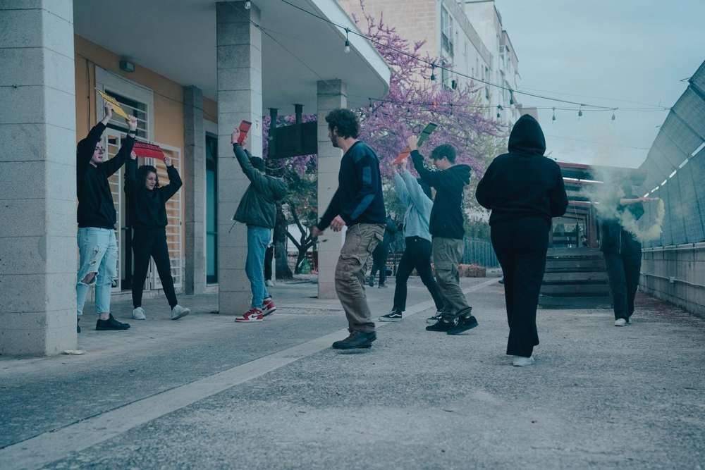 Performers carrying verb signs: Vendersi, Fondersi, Curarsi Performers carrying verb signs: Vendersi, Fondersi, Curarsi